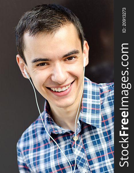 Portrait of handsome young man leaning casual on wall outside listening to music and smiling. Portrait of handsome young man leaning casual on wall outside listening to music and smiling