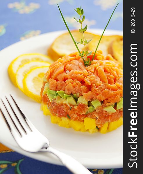 Fresh salmon tartar with avocado and pineapple in a white plate.