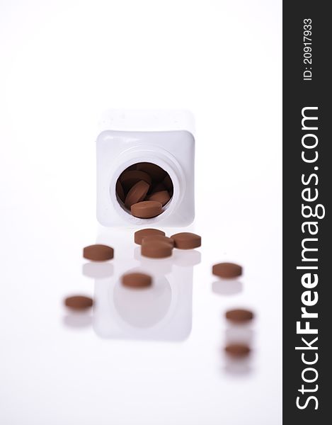 The inside of a white pill bottle with red generic pills on a white background. The inside of a white pill bottle with red generic pills on a white background.