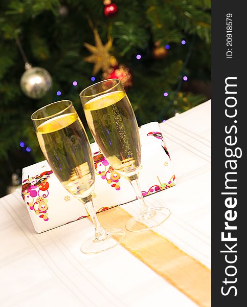 Two wine glasses with a present behind them and a christmas tree in the background. Two wine glasses with a present behind them and a christmas tree in the background