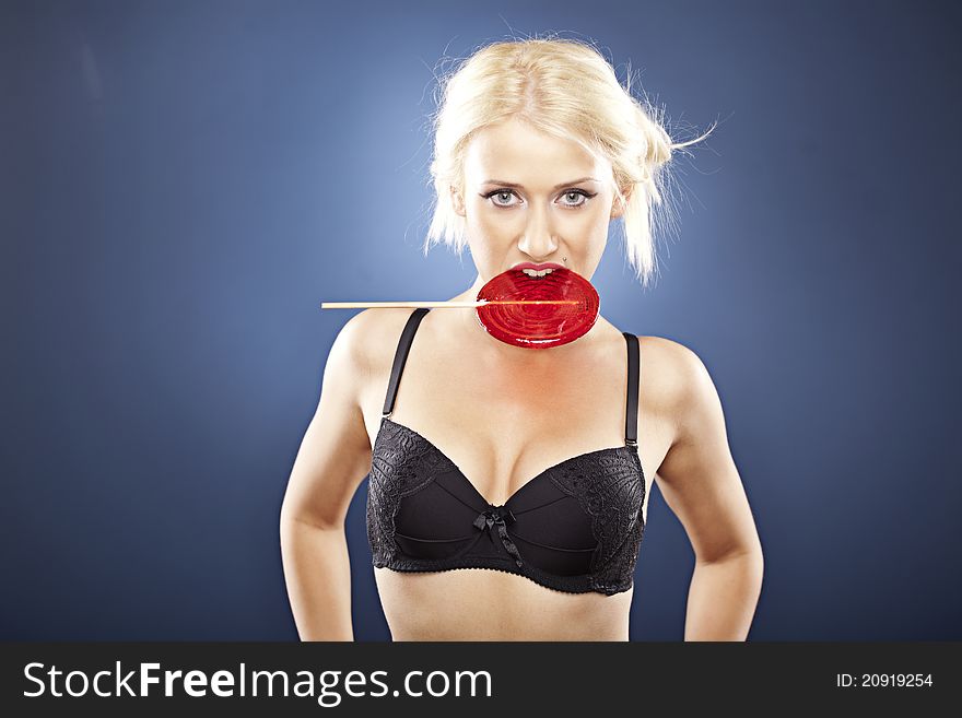 Beautiful blonde model bites into a red lollipop.
