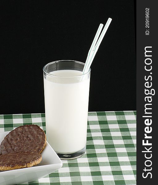 Glass of milk with chocolate coated cookies or biscuits on green gingham cloth. Glass of milk with chocolate coated cookies or biscuits on green gingham cloth