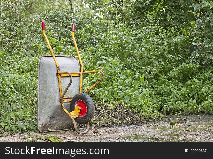 Wheelbarrow standing upright on concrete with foliage behind