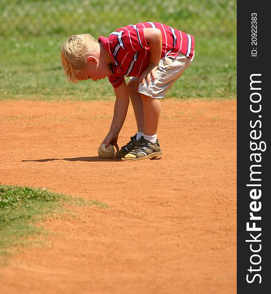 Young boy leaning over to pick up baseball. Young boy leaning over to pick up baseball