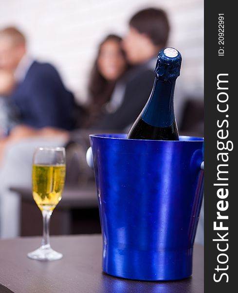 Champagne bottle in focus with glass filled, couples in background. Champagne bottle in focus with glass filled, couples in background