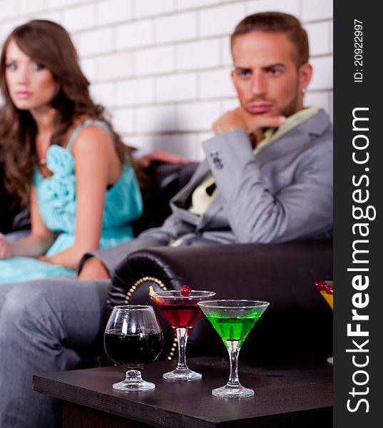 Annoyed young couple in the backround in bar or night club with colorful drinks in focus. Annoyed young couple in the backround in bar or night club with colorful drinks in focus.