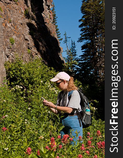 Image of a woman searching for a geocache with a GPS unit in the mountains