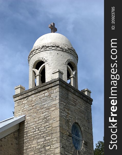 A stone and brick church tower with a cross reaches towards the blue sky.