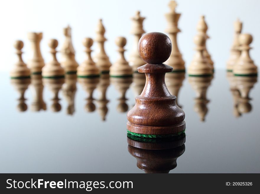 Darkly colored, wood pawn in front of light colored wooden chess pieces.