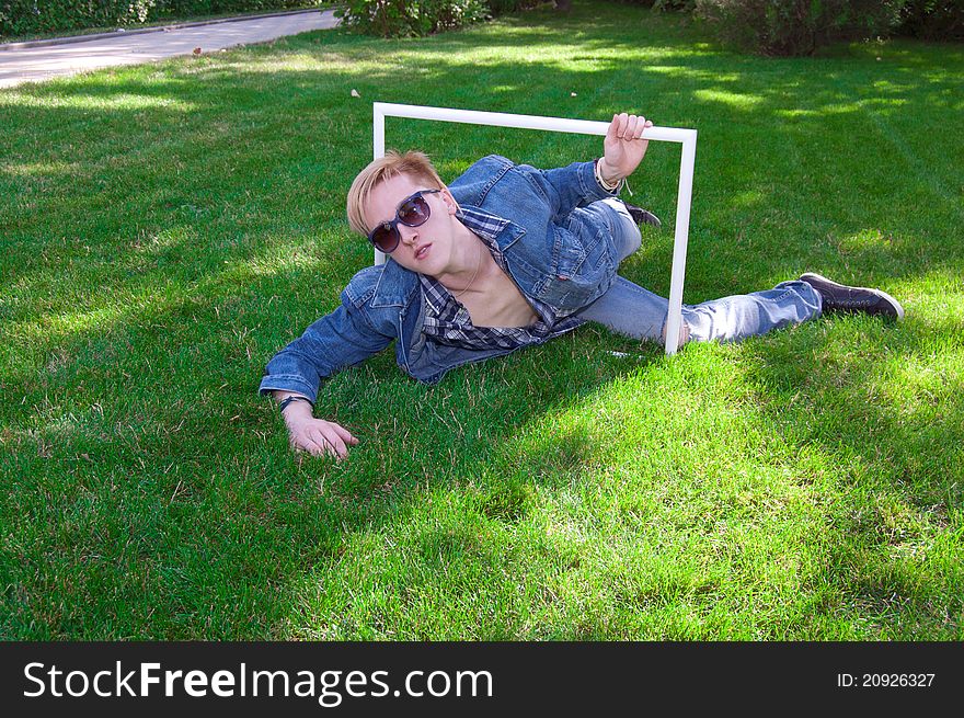 Young human on the green grass, he is wear jeans jacket, he has white frame and goggles. Young human on the green grass, he is wear jeans jacket, he has white frame and goggles
