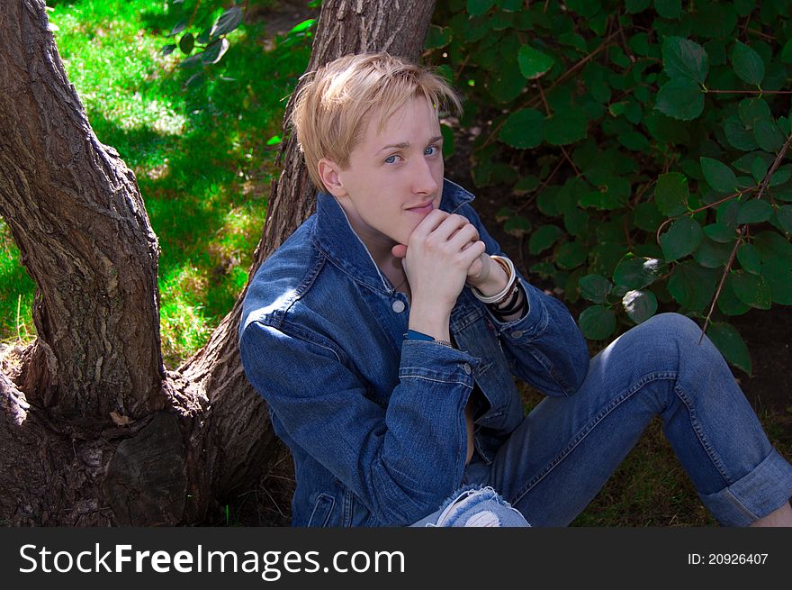 Young man in denim jacket relaxing by tree, summer scene. Young man in denim jacket relaxing by tree, summer scene.