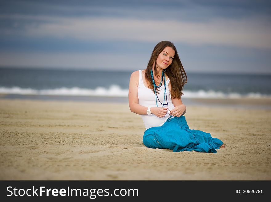 Beautiful young woman sits on sand near the ocean