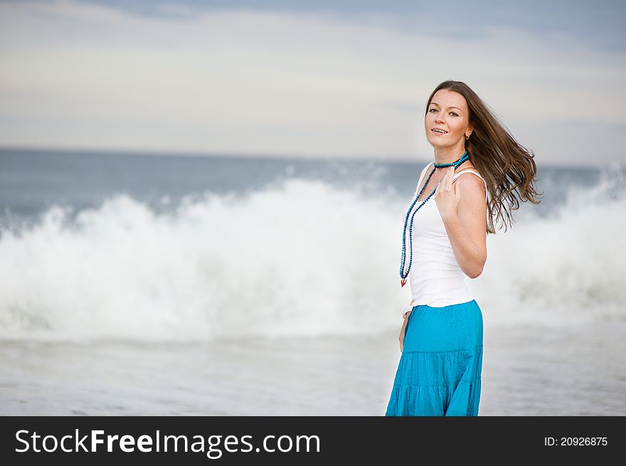 Beautiful young woman stands against the ocean