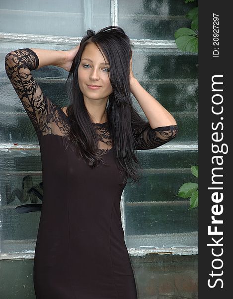 Female model wearing black dress. Girl with confident smile, standing near old window. Female model wearing black dress. Girl with confident smile, standing near old window.