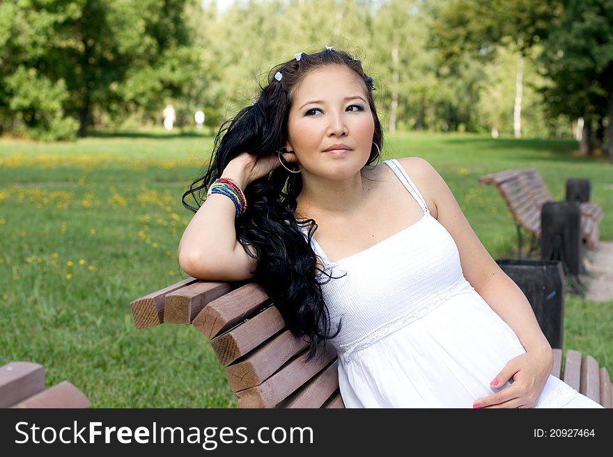 Beautiful pregnant girl sitting on bench in park