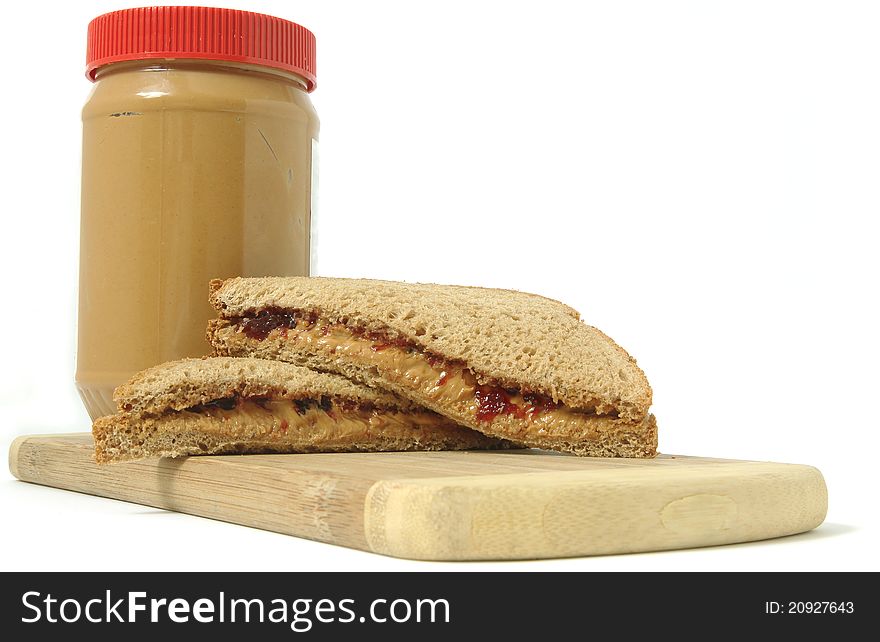 Peanut butter and jelly sandwich on a cutting board with a jar of peanut butter in the background, isolated on white.