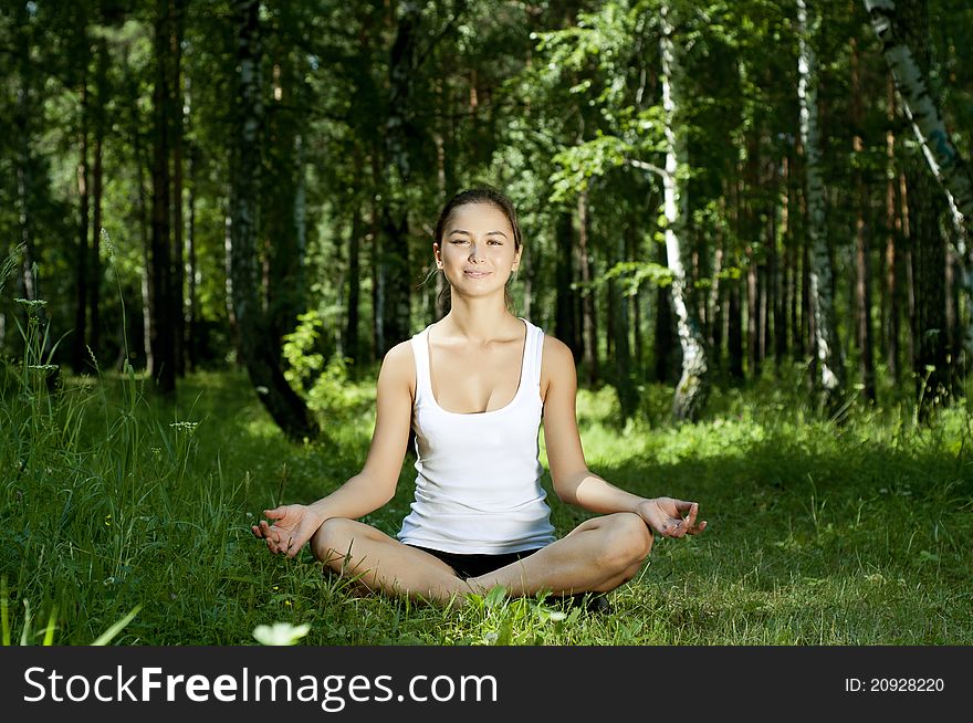 Young woman is engaged in yoga, in summer forest on a green grass. Young woman is engaged in yoga, in summer forest on a green grass