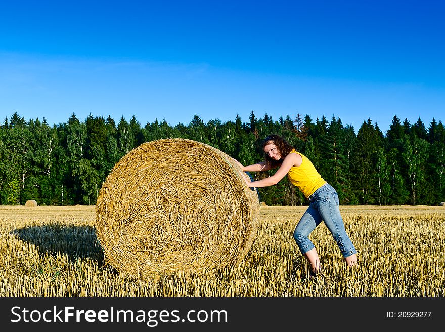Funny girl rolls a haystack in a field. Russia, Moscow region