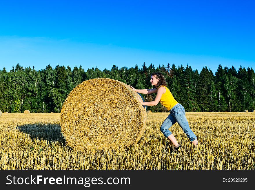 Funny girl rolls a haystack in a field