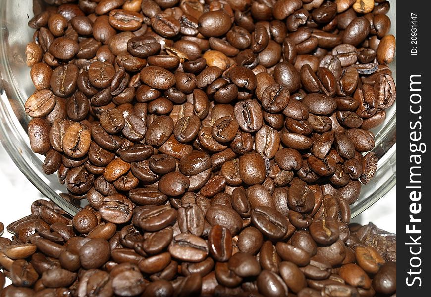 Coffee beans spilling over outside of the jar. .