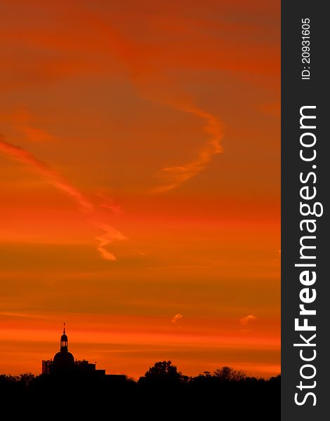 Silhouette of church dome and spire with treeline against orange and red striped clouds lining sunset sky. Silhouette of church dome and spire with treeline against orange and red striped clouds lining sunset sky