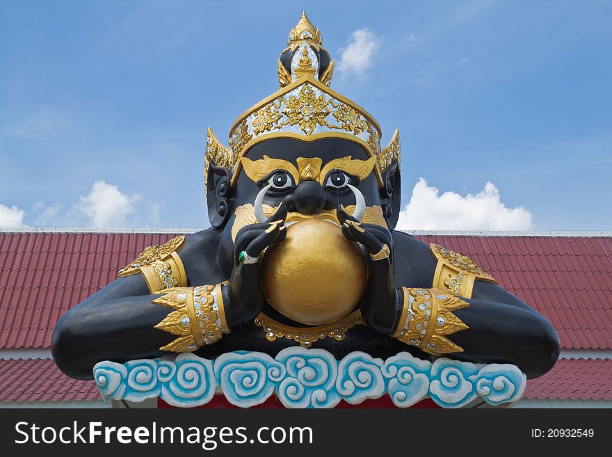 Statue of black deity called Rahu and blue sky background.