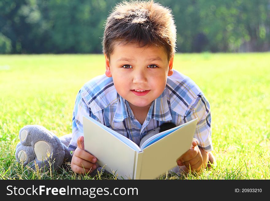The little boy lying on a green lawn reads the book. The little boy lying on a green lawn reads the book