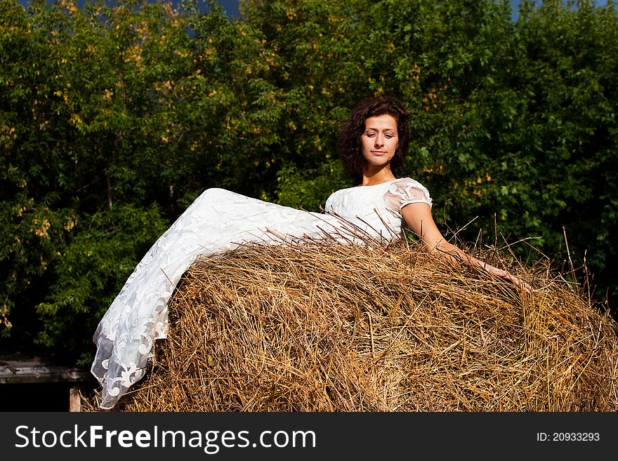 Brunette woman in white dress on hay in the woods