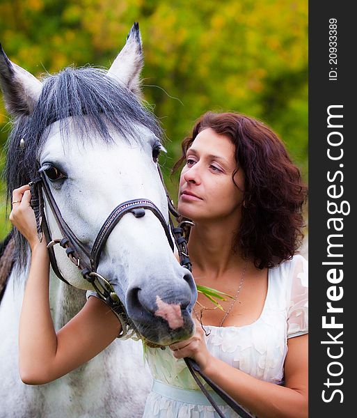 Beautiful woman in white with a horse in the park