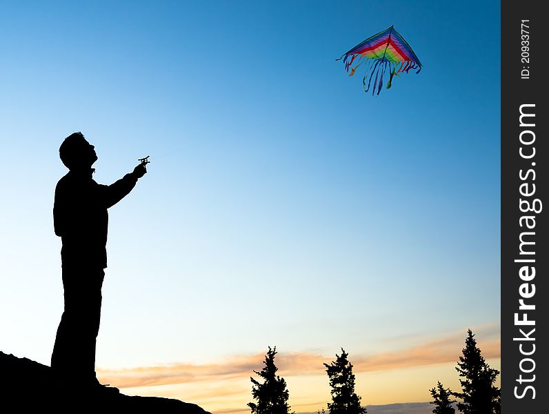 A young silhouette isolated man flying kite at a sunset summer day. A young silhouette isolated man flying kite at a sunset summer day