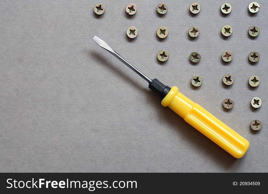 Industrial concept. Yellow screwdriver near lot of screws on gray surface with copy space. Industrial concept. Yellow screwdriver near lot of screws on gray surface with copy space