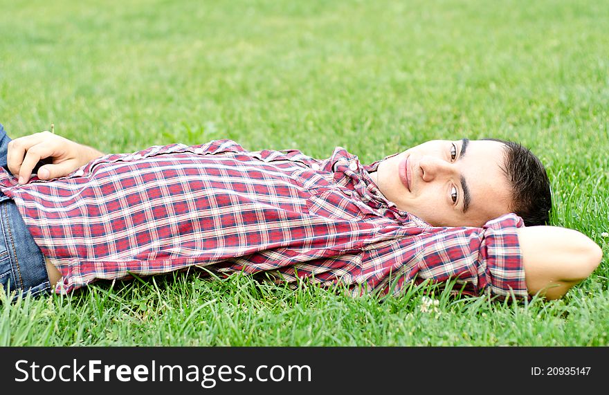 Young handsome man relaxing outdoors on the grass smiling looking at camera