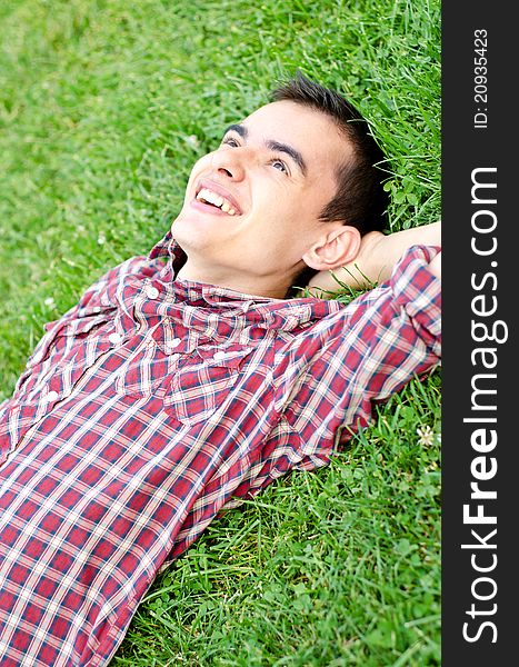 Young handsome man relaxing outdoors on the grass smiling looking at sky