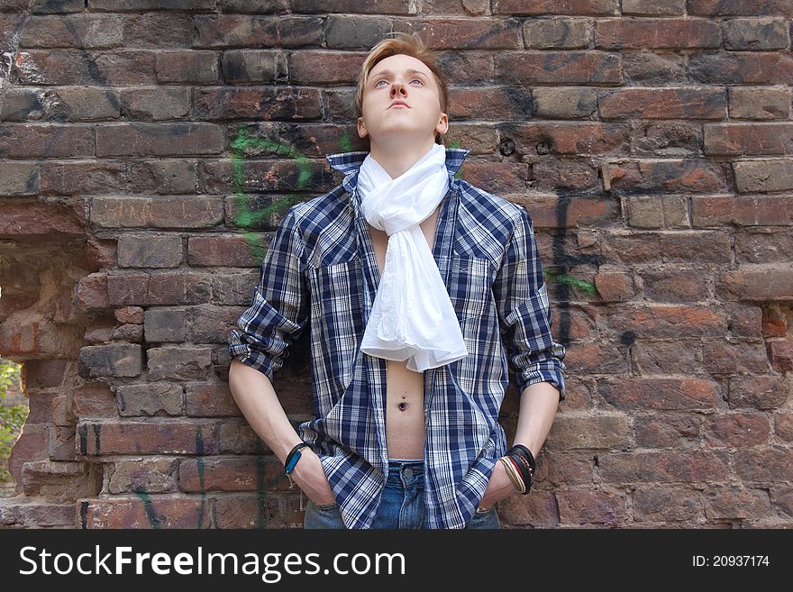 Young man standing near red brick wall. he has white scarf and blue shirt. he is looking up. Young man standing near red brick wall. he has white scarf and blue shirt. he is looking up