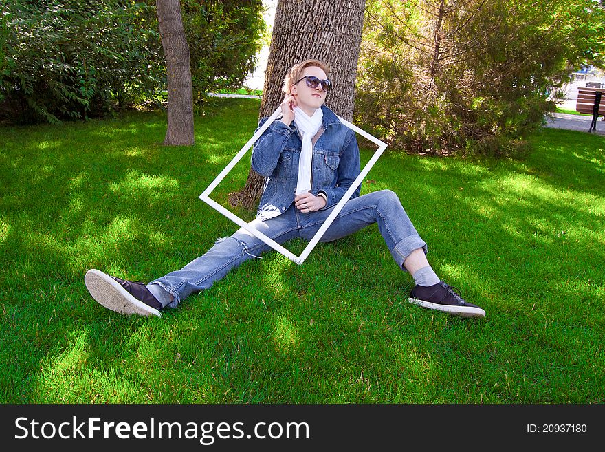 Young human on the green grass with white frame, he has blue goggles, jean jacket and white scarf