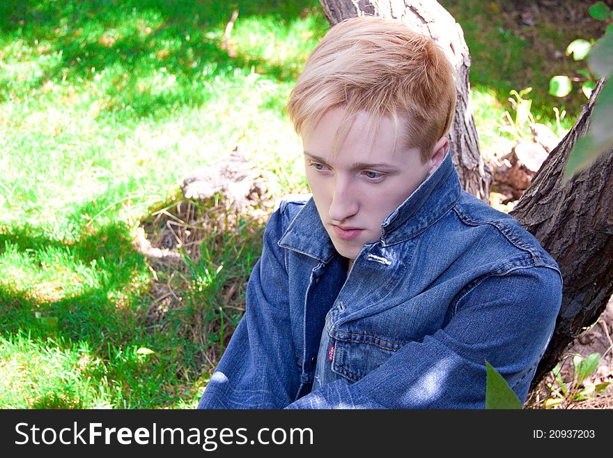 Young human on the green grass , he has jean jacket, he is near of tree