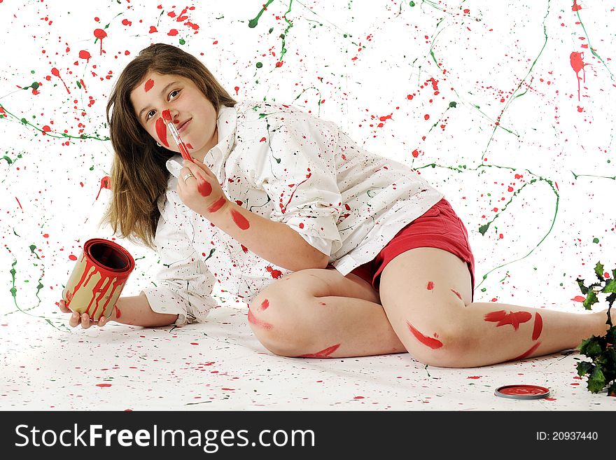 An attractive preteen painting her nose red while surrounded by white splattered with red and green paint. An attractive preteen painting her nose red while surrounded by white splattered with red and green paint.