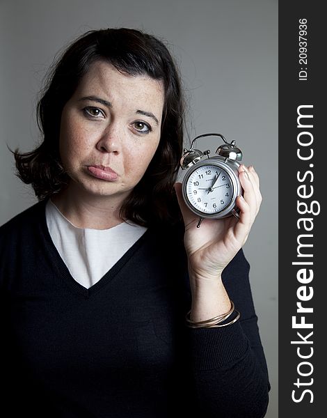 A woman holding a clock with an unhappy expression. A woman holding a clock with an unhappy expression.