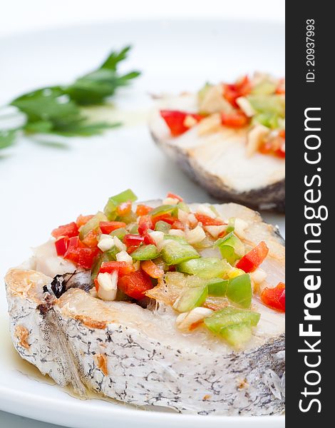 Hake fillets with peppers presented on a white background at lunchtime