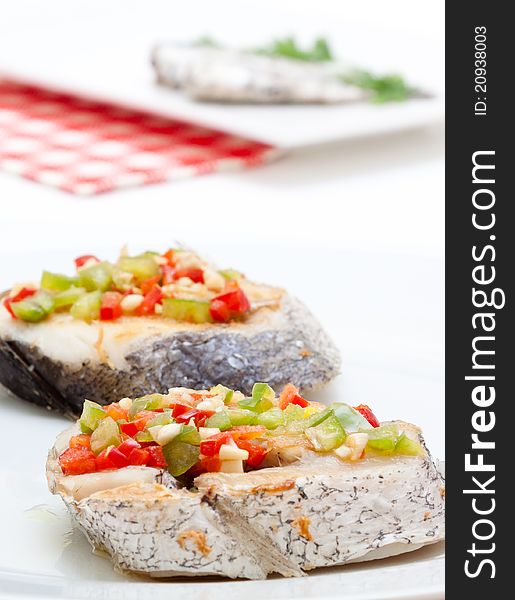 Hake fillets with peppers presented on a white background at lunchtime