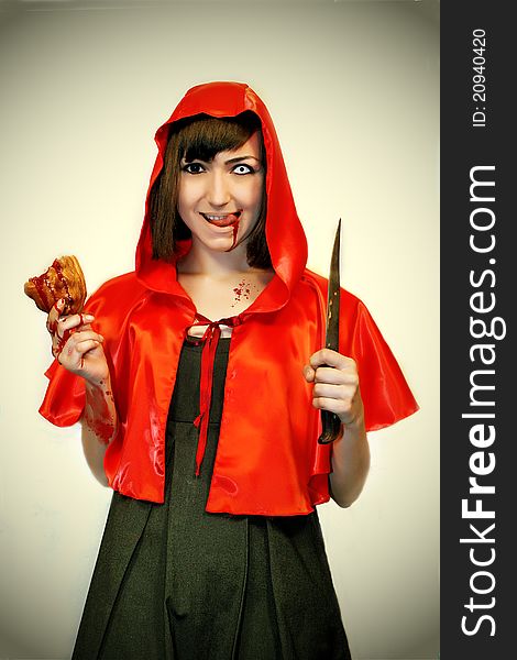 Model in studio malicious Little Red Riding Hood with a knife and a cake