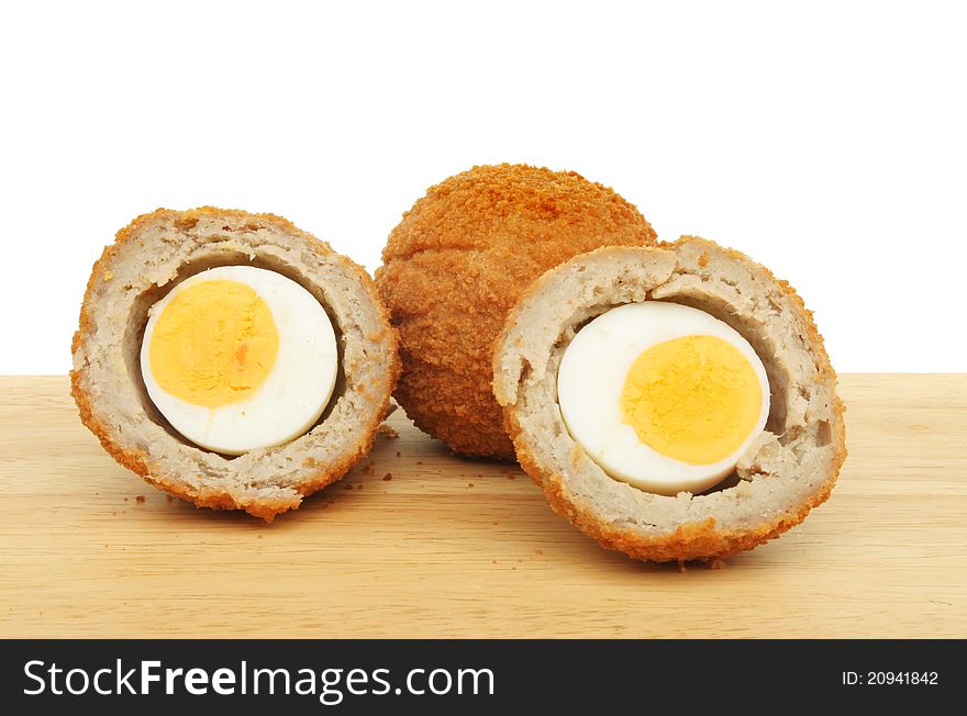 Whole and cut Scotch eggs on a wooden food preparation board