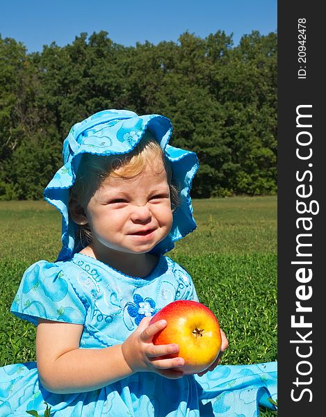 Funny little girl with a big apple in the meadow