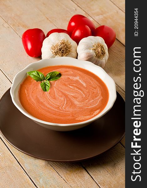 Photo of delicious tomato cream soup on wooden table with garlic and basil. Photo of delicious tomato cream soup on wooden table with garlic and basil