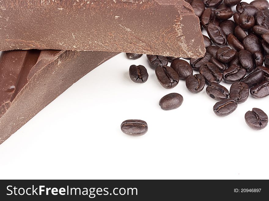 Bitter chocolate in pieces with coffee grains on a white background.