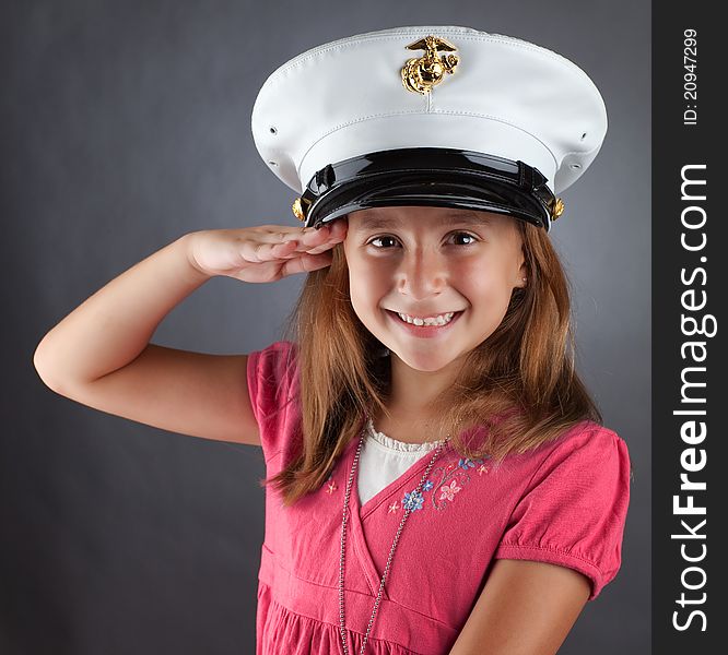 A patriotic girl salutes while wearing a military hat. A patriotic girl salutes while wearing a military hat