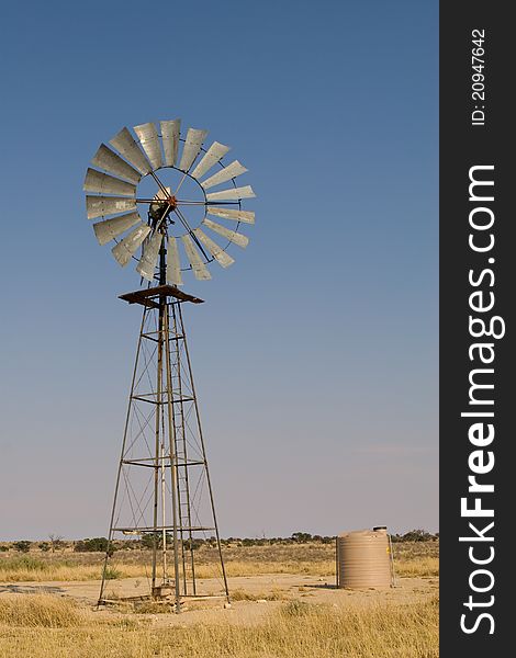 A vertical photograph of a windmill in the Kalahari desert with blue skies as background. A vertical photograph of a windmill in the Kalahari desert with blue skies as background