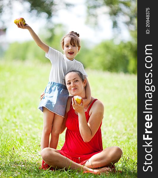 Beautiful young mother and her daughter eating pears in the park on a sunny summer day (focus on the women). Beautiful young mother and her daughter eating pears in the park on a sunny summer day (focus on the women)