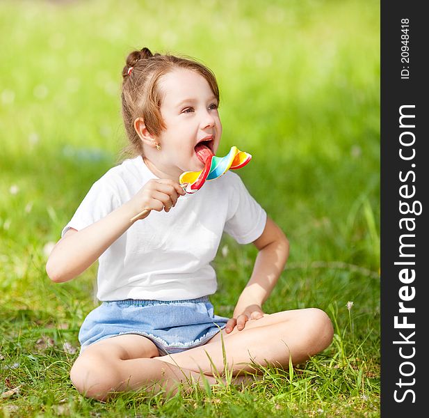 Cute little girl eating a lollipop on the grass in summertime. Cute little girl eating a lollipop on the grass in summertime