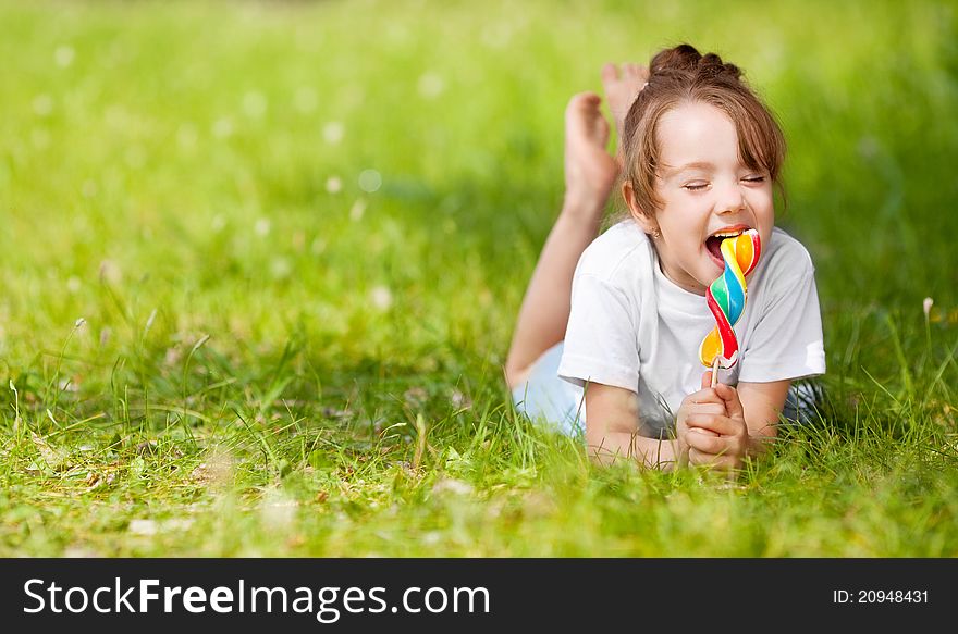 Cute little girl eating a lollipop on the grass in summertime. Cute little girl eating a lollipop on the grass in summertime